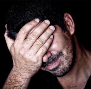 Un uomo con la mano a coprirsi gli occhi, in stato di disperazione